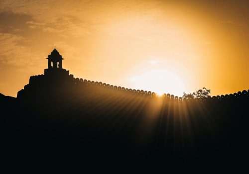 Silhouette of a historic fort in Jaipur, Rajasthan, India during sunrise with dramatic sunlight.